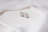 A pair of pearl button stud earrings placed on a white fabric surface.