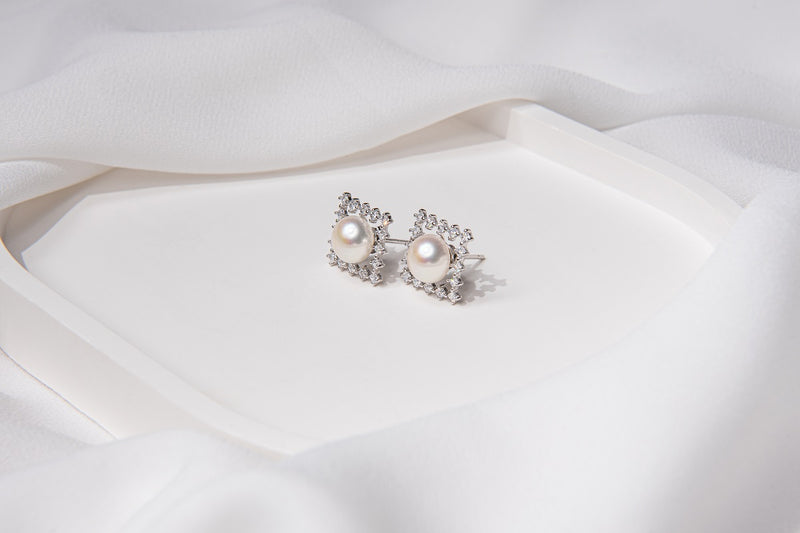 A pair of pearl button stud earrings placed on a white fabric surface.