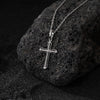 Silver cross pendant on a chain against a dark stone background