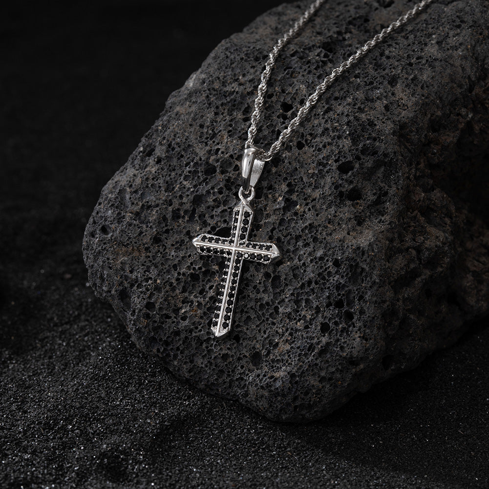 Silver cross pendant on a chain against a dark stone background