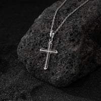 Silver cross pendant on a chain against a dark stone background