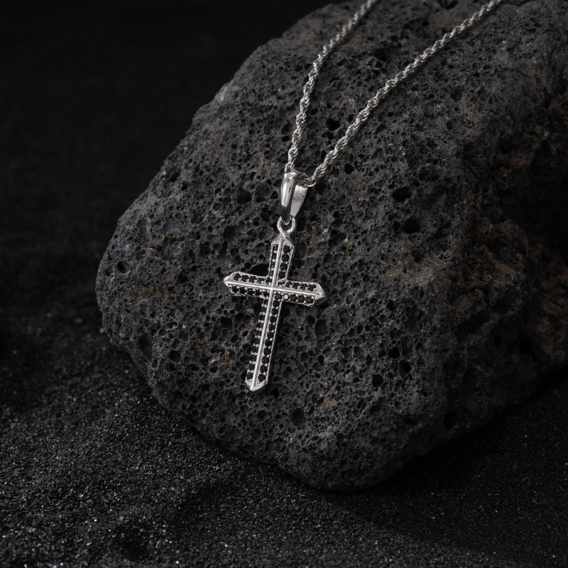 Silver cross pendant on a chain against a dark stone background