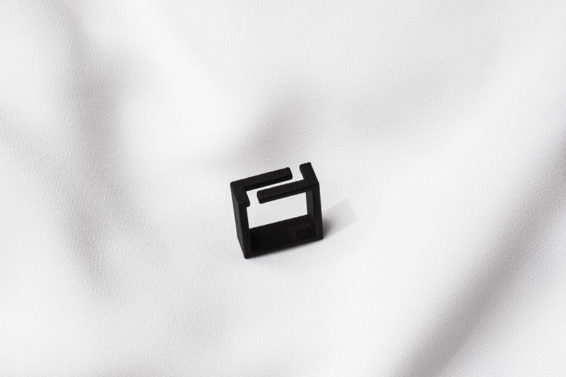 A matte black ring with a minimalist design, placed on a white textured surface.