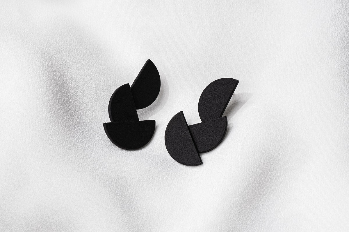 A pair of matte black earrings with a minimalist design, consisting of three connected semi-circular shapes.