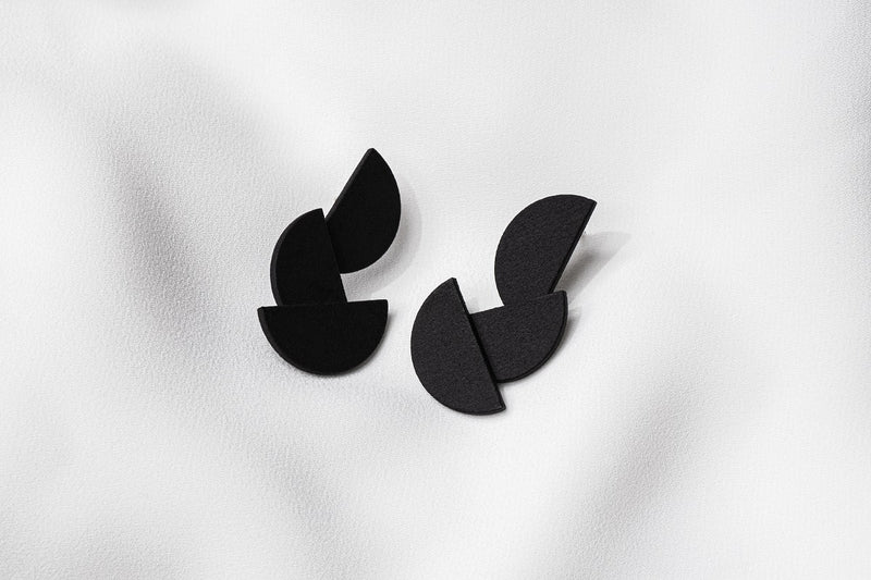 A pair of matte black earrings with a minimalist design, consisting of three connected semi-circular shapes.
