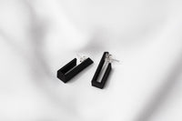 A pair of matte black earrings with a minimalist design, on a white background