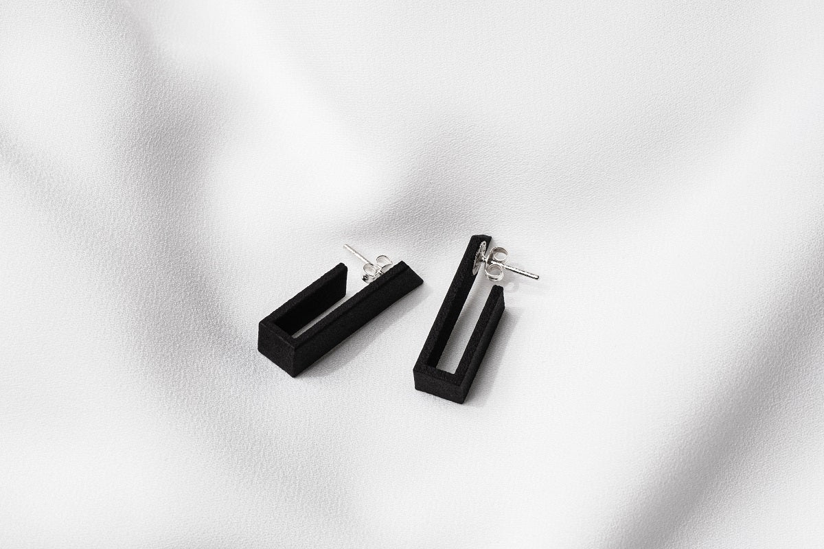 A pair of matte black earrings with a minimalist design, on a white background