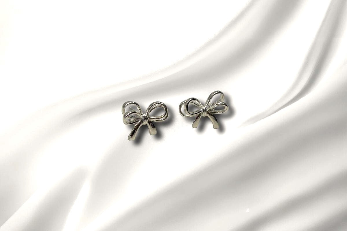 A pair of sterling silver bow shaped stud earrings with butterfly backs, displayed on a white silky surface.