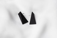 A pair of matte black, triangular earrings on a white background.