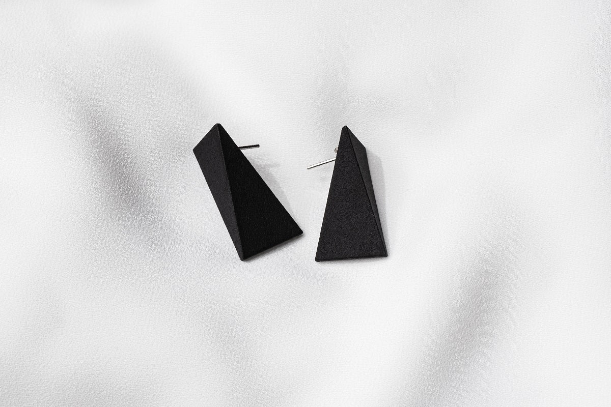 A pair of matte black, triangular earrings on a white background.