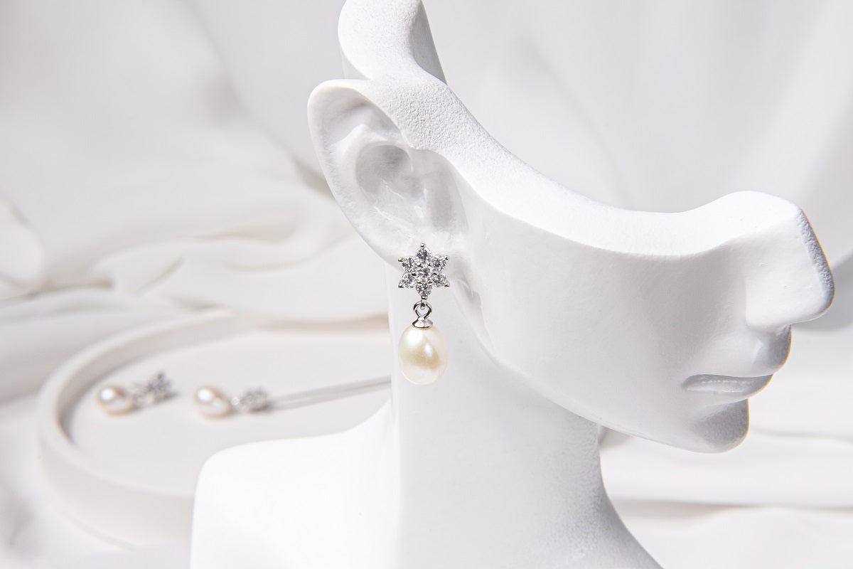 A set of sterling silver jewelry including a pendant with a drop shape pearl and flower diamond cubic zirconia, along with a pair of earrings with a similar design, displayed on a white surface.