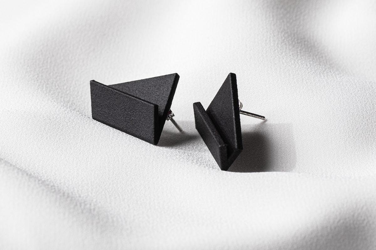 A pair of matte black, geometric drop earrings with a matte finish, lying on a white fabric surface.