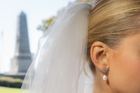 A pair of pearl earrings with butterfly backs and dangle design, featuring white pearls and a sparkling floral-shaped pendant and diamond cubic zirconia. Worn by a female model.