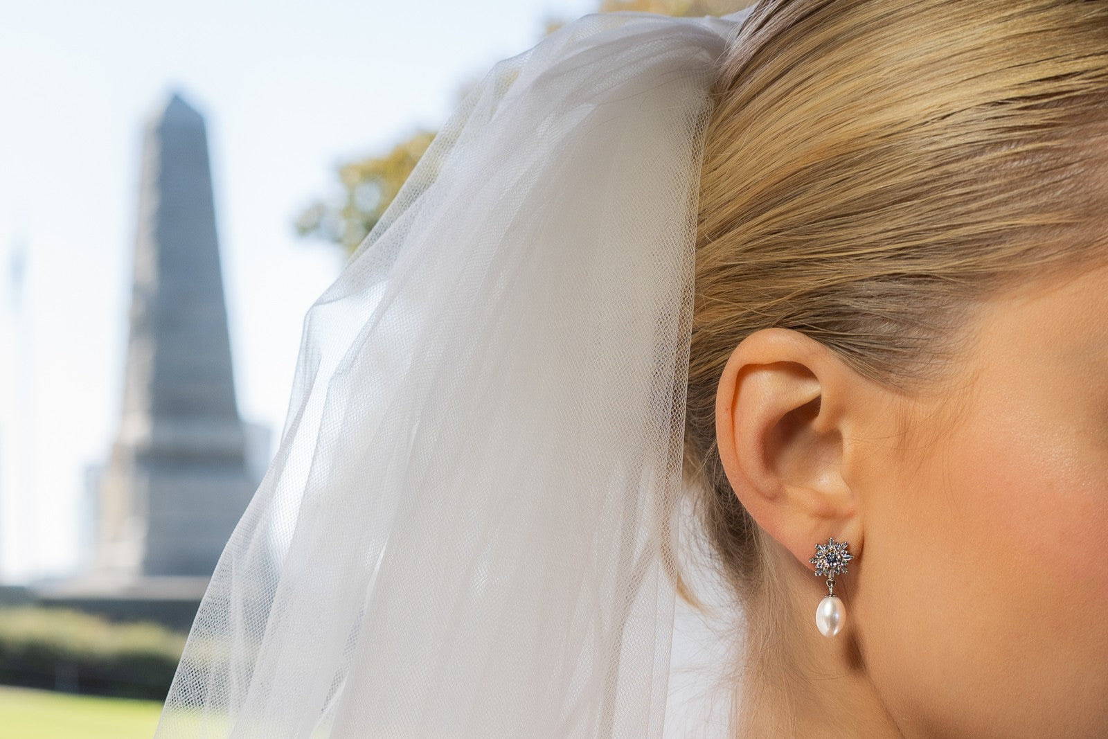 A pair of pearl earrings with butterfly backs and dangle design, featuring white pearls and a sparkling floral-shaped pendant and diamond cubic zirconia. Worn by a female model.