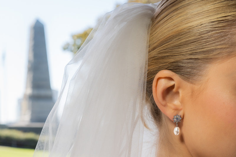 A pair of pearl earrings with butterfly backs and dangle design, featuring white pearls and a sparkling floral-shaped pendant and diamond cubic zirconia. Worn by a female model.