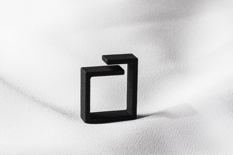 A matte black ring with a minimalist design, displayed on a white textured surface.