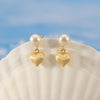 Gold heart-shaped earrings with pearls on a shell against a blue sky background