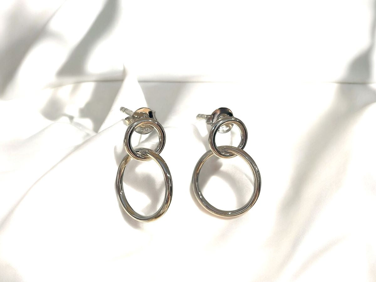 A pair of silver stud hoop earrings with butterfly backs, placed on a white textured surface.