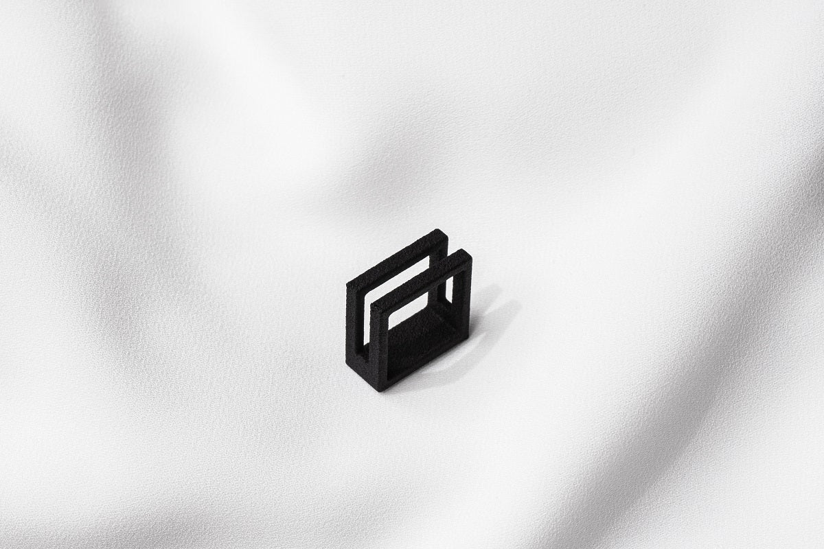 A matte black ring with a minimalist design, placed on a white textured surface.