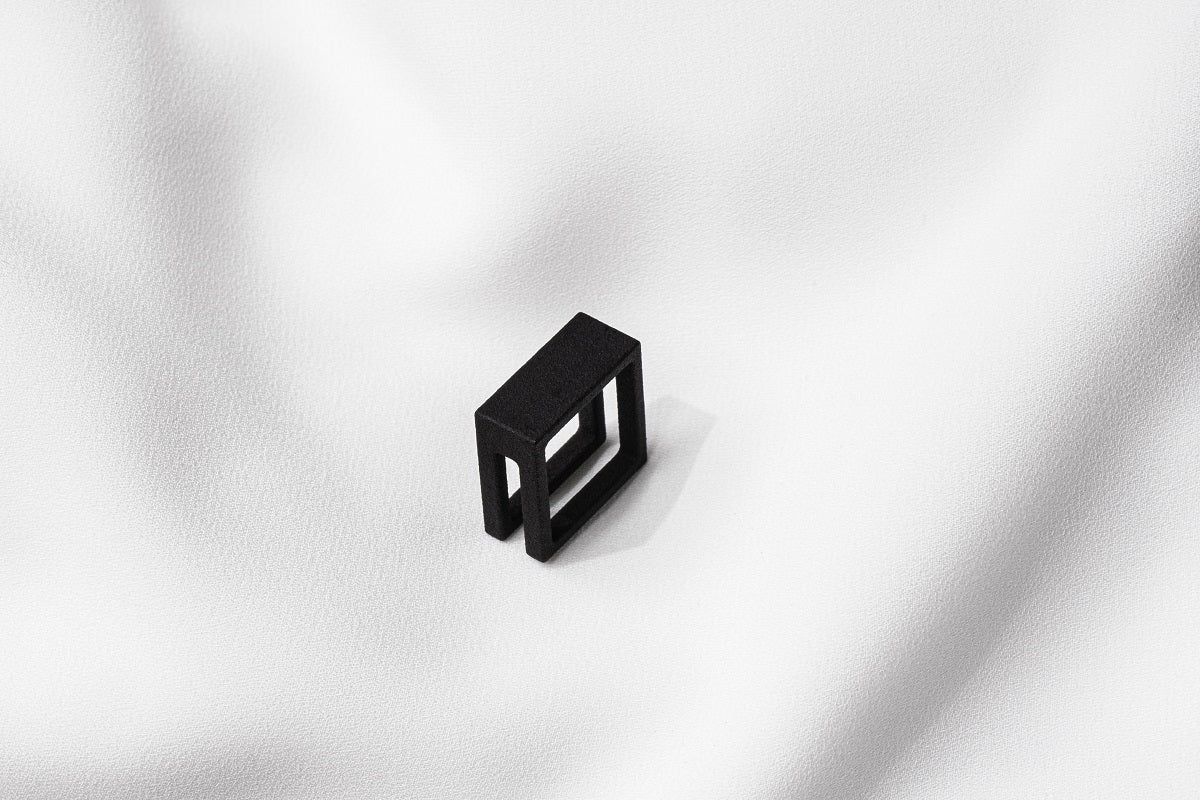 A matte black ring with a minimalist design, placed on a white textured surface.