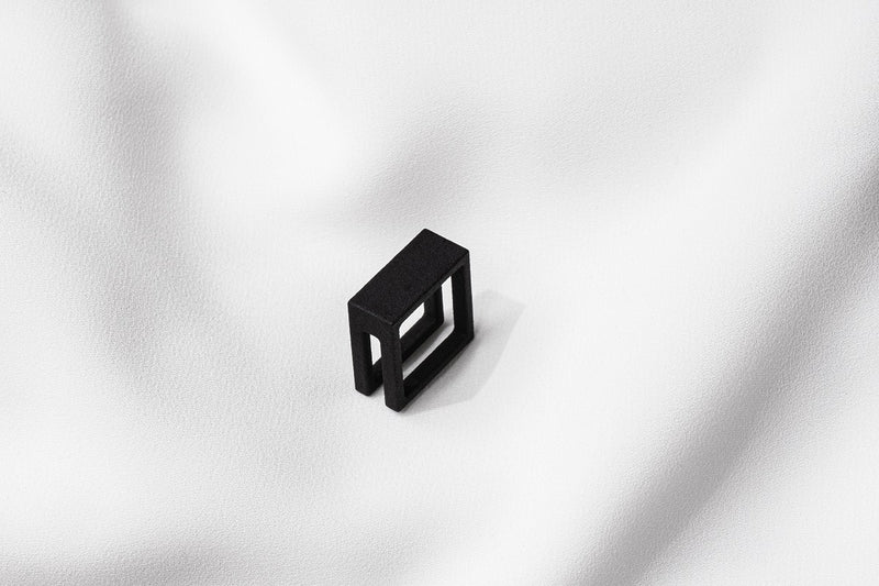 A matte black ring with a minimalist design, placed on a white textured surface.