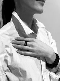 Person wearing a black ring on a white shirt against a gray background