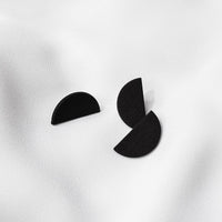 A pair of matte black modular earrings with one larger semicircular piece and one smaller, placed against a white background.