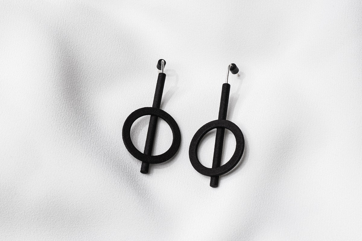 A pair of matte black earrings with a minimalist design, consisting of two overlapping circles on a white background.