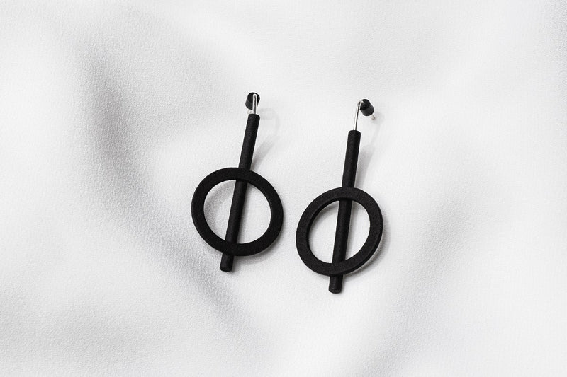 A pair of matte black earrings with a minimalist design, consisting of two overlapping circles on a white background.