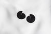 A pair of matte black Pacman-shaped earrings placed on a white surface.