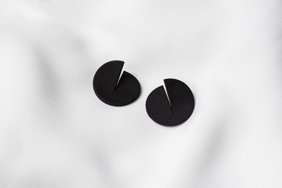 A pair of matte black Pacman-shaped earrings placed on a white surface.