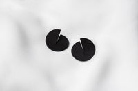 A pair of matte black Pacman-shaped earrings placed on a white surface.