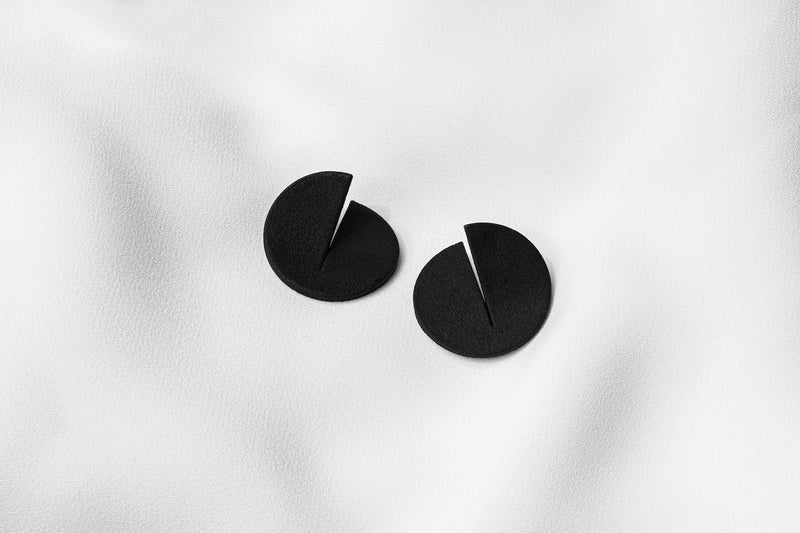 A pair of matte black Pacman-shaped earrings placed on a white surface.