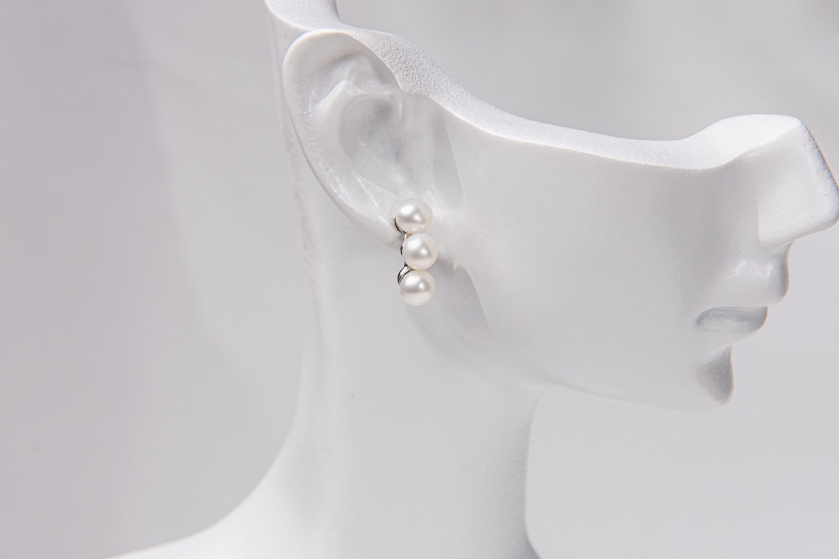 A pair of pearl earrings with a butterfly backs on a mannequin head.