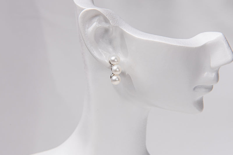 A pair of pearl earrings with a butterfly backs on a mannequin head.