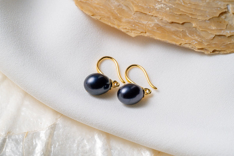A pair of dangle darn blue pearl hook earrings in gold vermeil, placed on a white surface with a shell in the background