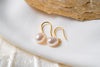 A pair of dangle pearl hook earrings in gold vermeil, placed on a white surface with a shell in the background
