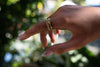 Hand wearing a gold bubble design ring with a blurred natural background
