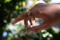 Hand wearing a gold bubble design ring with a blurred natural background