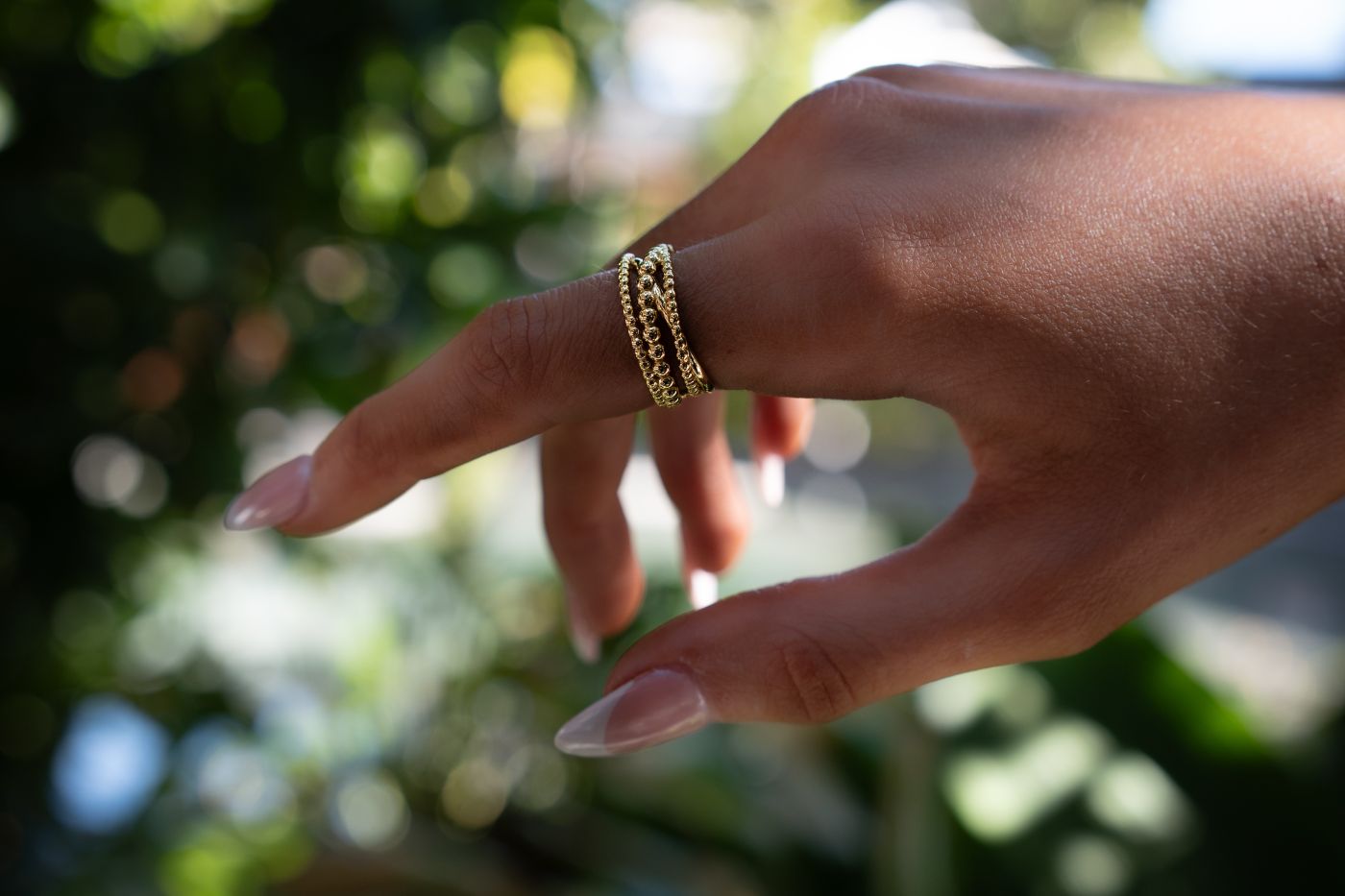 Hand wearing a gold bubble design ring with a blurred natural background