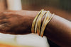 Close-up of a wrist with multiple gold bracelets on a blurred background