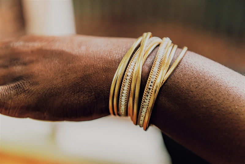 Close-up of a wrist with multiple gold bracelets on a blurred background
