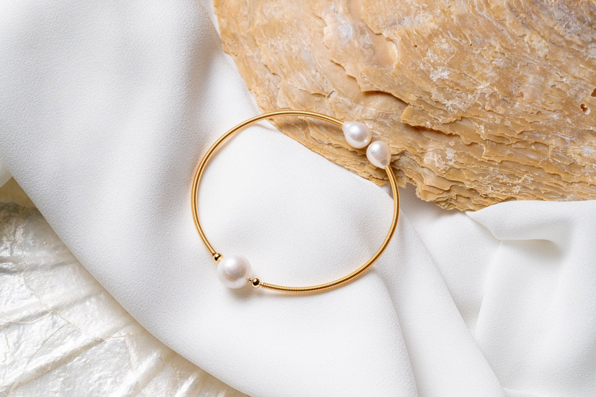 A gold and pearl bracelet on a white and seashell background