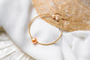 A gold and champagne pearl bracelet on a white and seashell background