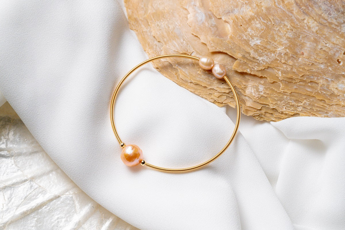 A gold and champagne pearl bracelet on a white and seashell background
