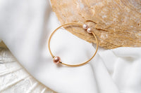 A gold and rose pearl bracelet on a white and seashell background