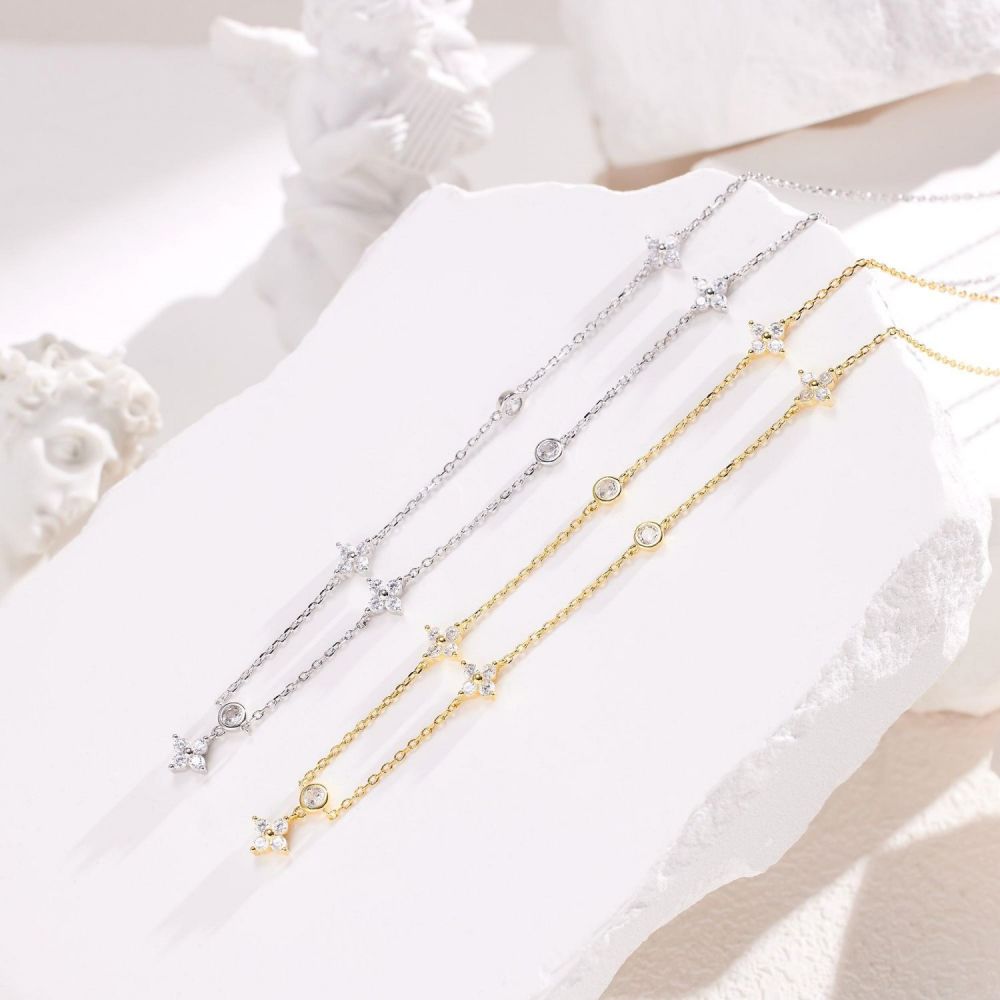 Two Troika necklaces laid out, one with a silver chain and silver charms, and the other with a gold vermeil chain and gold vermeil charms. Both are adorned with diamond cubic zirconia pendants.