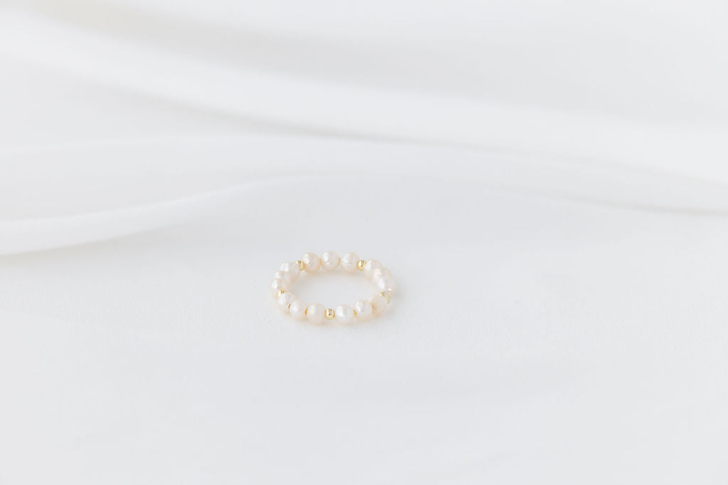 An elegant gold and pearl ring on a white background