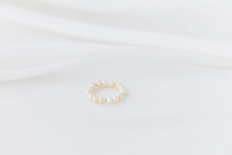 An elegant gold and pearl ring on a white background