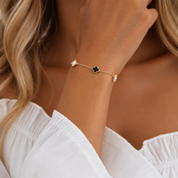 A gold chain bracelet with black four-leaf clover and small white mother of pearl, shown worn on a woman's wrist.